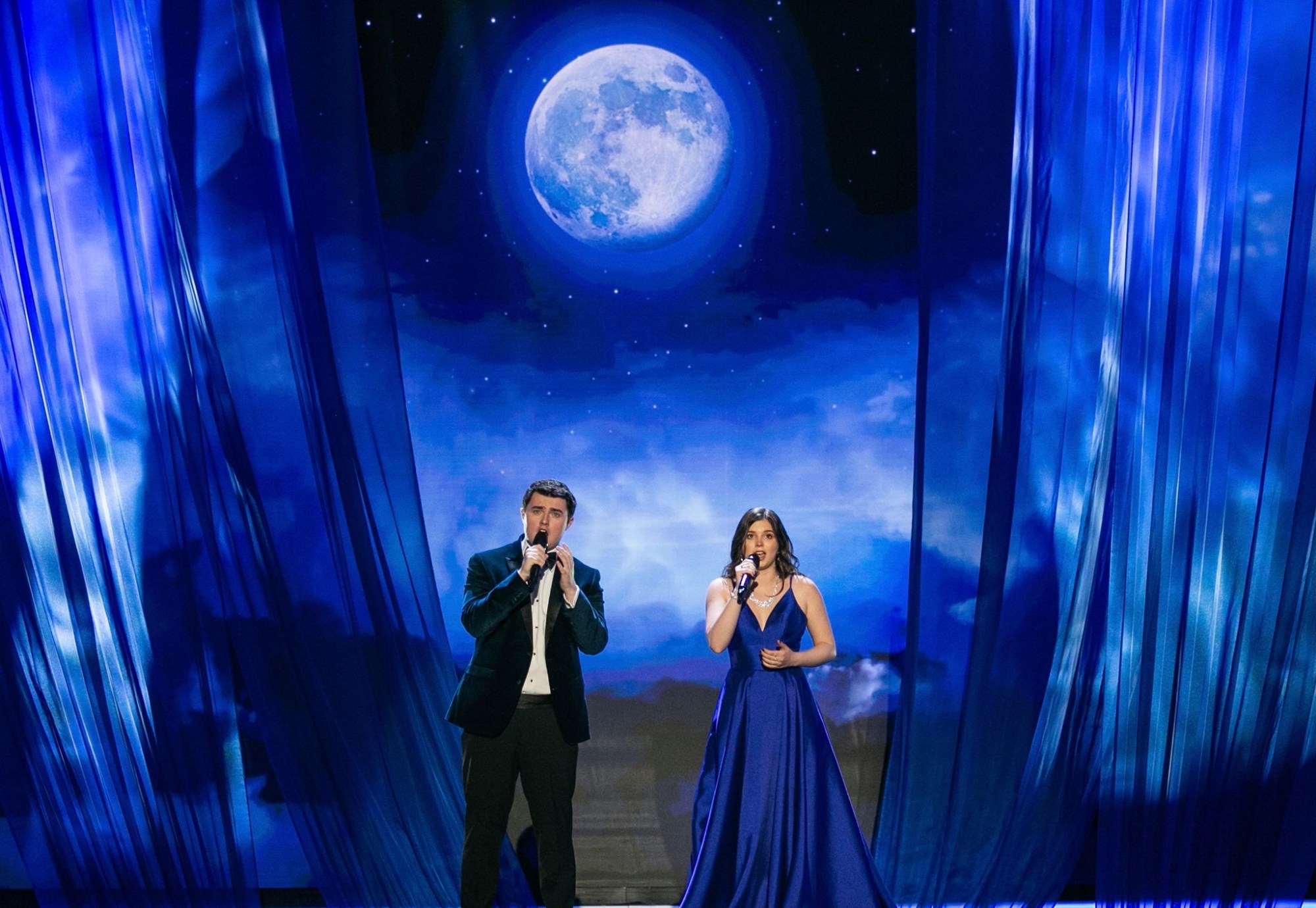 Bello Duo performing on stage beneath a moonlit backdrop